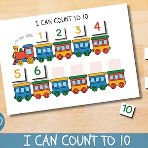 Könnte beinhalten: Ein farbenfroher Lehrdruck mit dem Titel "I Can Count to 10" zeigt einen Zug mit nummerierten Waggons. Einzelne Zahlenkacheln sind um den Druck herum platziert. Der Druck befindet sich auf weißem Hintergrund.