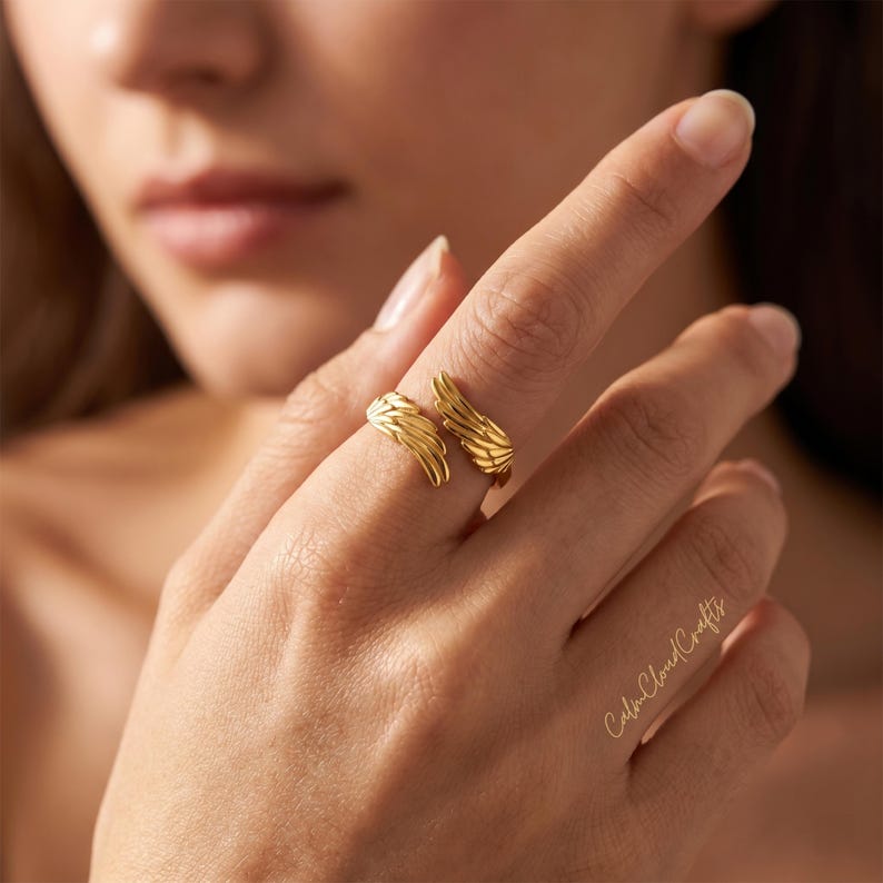 Puede incluir: Un anillo dorado con un dise&ntilde;o de alas. El anillo se lleva en un dedo, con las alas envolviendo el dedo. El anillo est&aacute; hecho de un material met&aacute;lico brillante. Es una pieza de joyer&iacute;a.
