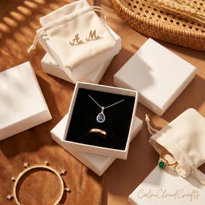Puede incluir: Una variedad de joyas, que incluyen un collar con colgante de zafiro, un anillo de oro y una pulsera con detalles en forma de estrella. Las joyas se exhiben en cajas blancas y peque&ntilde;as bolsas con cord&oacute;n. El texto "Calm Cloud Crafts" es visible.