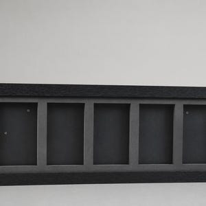 May include: A rectangular black picture frame with five openings. The frame has a dark gray interior and a textured, dark wood-like exterior. The frame is designed to hold multiple photos or artwork.
