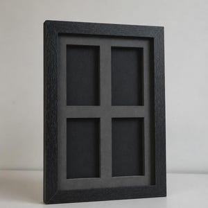 May include: A black multi-photo frame with four openings. The frame has a textured, dark gray finish and a gray matting around the photo openings. The frame is designed to hold four photos and is suitable for displaying memories or artwork.