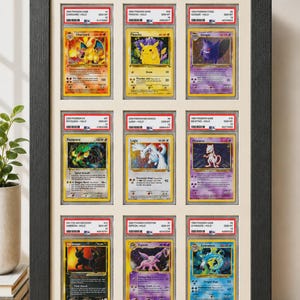 May include: Framed display of nine Pok&eacute;mon trading cards, including Charizard, Pikachu, and Gengar. The cards are encased in protective holders and arranged in a black frame, showcasing various colorful illustrations.