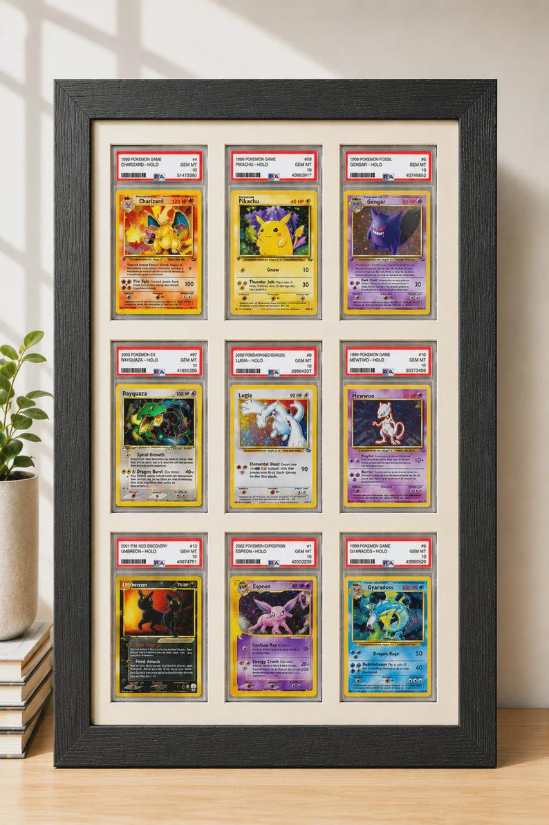May include: Framed display of nine Pok&eacute;mon trading cards, including Charizard, Pikachu, and Gengar. The cards are encased in protective holders and arranged in a black frame, showcasing various colorful illustrations.