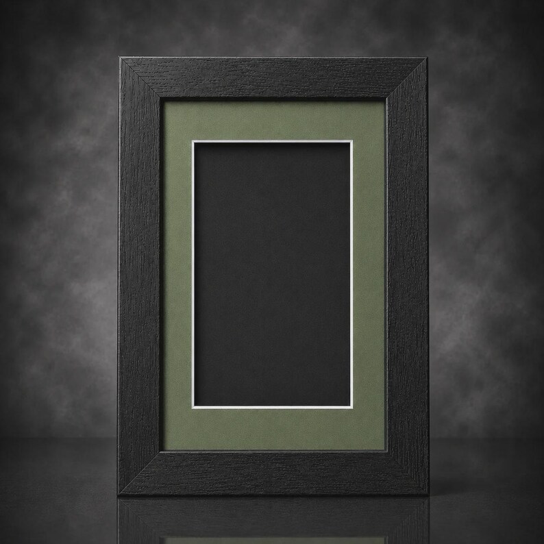 May include: A rectangular black picture frame with a green mat and white border. The frame is empty, with a black interior. The frame is made of wood and has a simple, modern design. The frame is suitable for displaying photos or artwork.