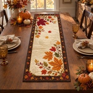May include: A rectangular fabric table runner featuring a cream-colored center with embroidered autumn leaves in shades of red, orange, and green, surrounded by a dark brown border decorated with a repeating pattern of small colorful fall foliage.