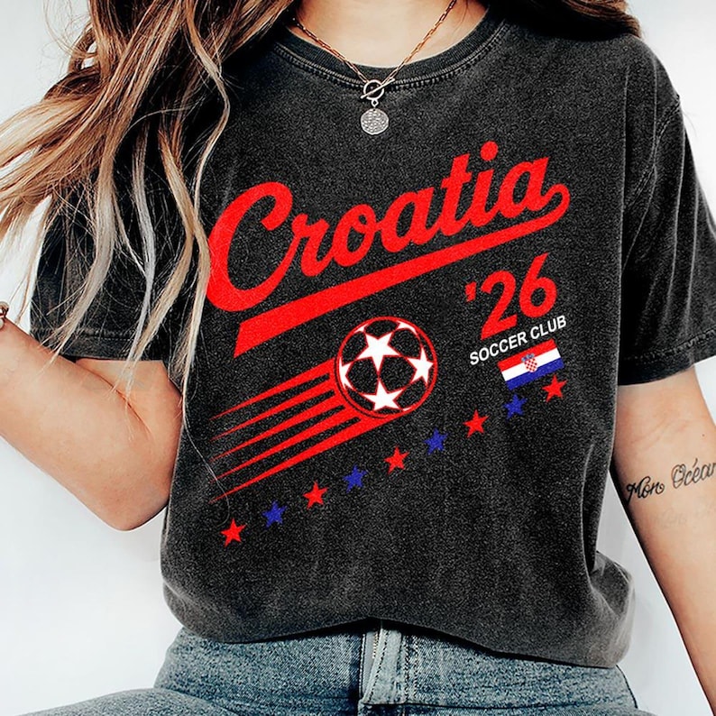 Puede incluir: Una camiseta de manga corta gris carb&oacute;n con el texto rojo Croatia, el n&uacute;mero 26 y las palabras SOCCER CLUB. El dise&ntilde;o incluye un gr&aacute;fico de un bal&oacute;n de f&uacute;tbol con l&iacute;neas de movimiento, una peque&ntilde;a bandera croata y una fila de estrellas rojas y azules.