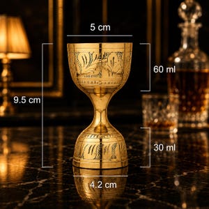 May include: A gold-colored, engraved metal shot glass, 9.5 cm tall and 5 cm wide, with a capacity of 60 ml. The base is 4.2 cm wide and holds 30 ml. The glass features an etched floral design.