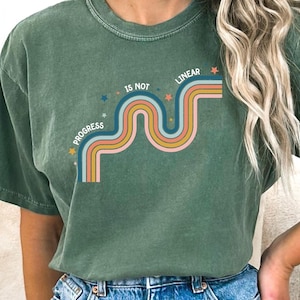 May include: A green t-shirt with a retro-style graphic that says "Progress is not linear" with a wavy rainbow design and stars.