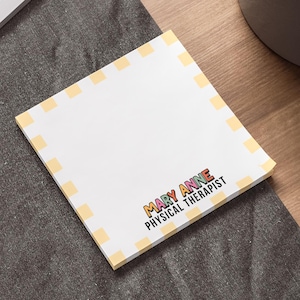 May include: A white notepad with a yellow and white checkered border. The notepad has the text "MARY ANNE PHYSICAL THERAPIST" printed on it in colorful letters.