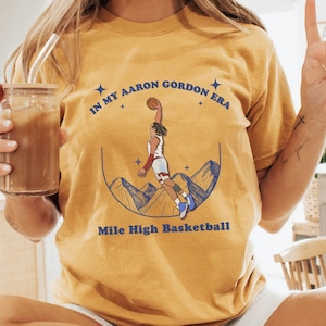 May include: A yellow t-shirt with a basketball player graphic and the text "In my Aaron Gordon Era Mile High Basketball".