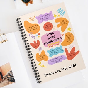 以下が含まれることがあります： カラフルなデザインと表紙に「BCBA Daily Affirmations」というテキストが書かれた、スパイラルバインディングされたノート。このノートは、行動分析士のための肯定的なアファメーションでいっぱいです。