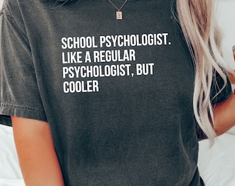 May include: A dark gray t-shirt with the text "SCHOOL PSYCHOLOGIST. LIKE A REGULAR PSYCHOLOGIST, BUT COOLER" printed in white.