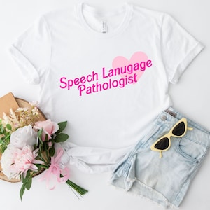 Peut inclure: T-shirt blanc avec un cœur rose et le texte "Speech Language Pathologist" en lettres roses.