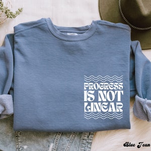 May include: A blue sweatshirt with a white graphic that says "Progress is not linear" in a retro font.