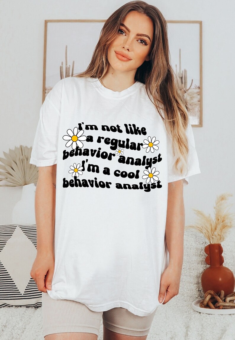 K&ouml;nnte beinhalten: Wei&szlig;es T-Shirt mit einem schwarzen Aufdruck, auf dem steht "Ich bin nicht wie ein normaler Verhaltensanalytiker Ich bin ein cooler Verhaltensanalytiker" mit wei&szlig;en G&auml;nsebl&uuml;mchen um den Text herum.