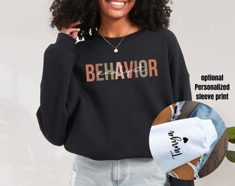 Puede incluir: Sudadera negra con la palabra "BEHAVIOR ANALYST" en un diseño multicolor en el pecho. La manga tiene una impresión personalizada opcional. La sudadera es de estilo casual.