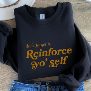 May include: Black sweatshirt with the text "don't forget to Reinforce yo' self" in gold lettering.