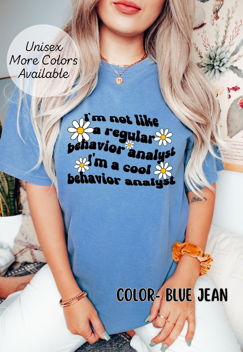 K&ouml;nnte beinhalten: Ein T-Shirt in Jeansblau mit einem wei&szlig;en G&auml;nsebl&uuml;mchen-Motiv und dem Text "Ich bin nicht wie ein normaler Verhaltensanalytiker Ich bin ein cooler Verhaltensanalytiker".
