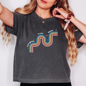 May include: Dark gray t-shirt with the text "progress is not linear" in a retro rainbow design. The design features a wavy line with blue, pink, yellow, and orange stripes, and small star accents. A casual, comfortable tee.