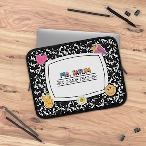 May include: Black and white composition notebook-style laptop sleeve with the text "MS. TATUM 3RD GRADE TEACHER." The sleeve has a white frame and colorful stickers, including a pink heart, peace sign, shooting star, and smiley face.