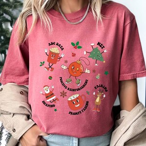 May include: Red t-shirt with a Christmas-themed graphic featuring cartoon characters representing different teaching methods. The text on the shirt reads "ABC Data, Net, Positive Reinforcement, Pairing, Shaping, Prompt Fading".