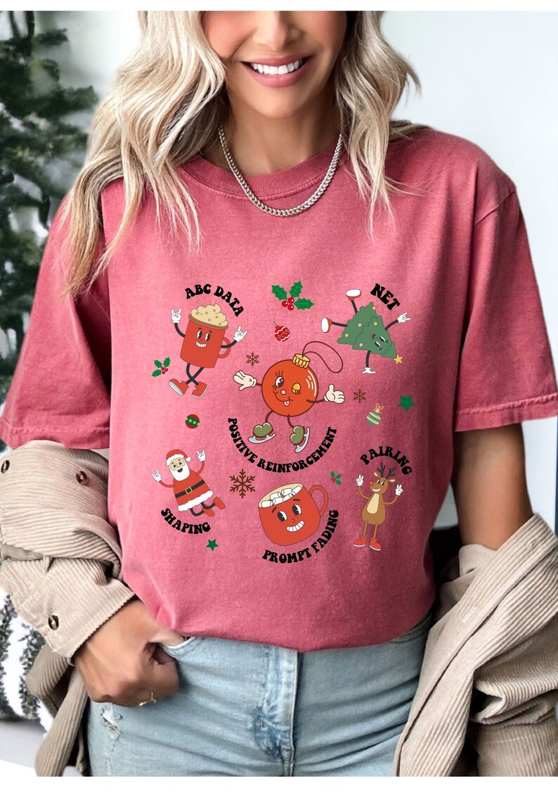 May include: Red t-shirt with a Christmas-themed graphic featuring cartoon characters representing different teaching methods. The text on the shirt reads "ABC Data, Net, Positive Reinforcement, Pairing, Shaping, Prompt Fading".