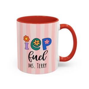 Könnte beinhalten: Eine weiße Keramiktasse mit rotem Innenraum und Henkel. Die Tasse hat ein rosa-weiß gestreiftes Muster und die Worte "IEP fuel" in bunten, floral dekorierten Buchstaben. Der Name "MS. TERRY" ist darunter aufgedruckt.