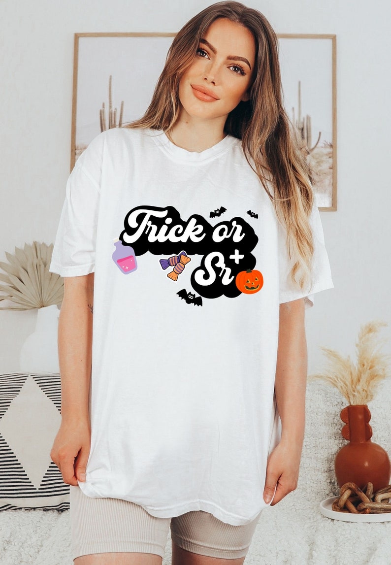 Puede incluir: Camiseta blanca con un gr&aacute;fico negro que dice "Trick or Sr+" con una botella de poci&oacute;n morada, caramelos y una calabaza.