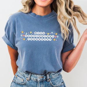 Könnte beinhalten: Ein blaues T-Shirt mit dem Text "NICU Respiratory Therapist" in weißen Buchstaben auf einer Schnur mit bunten Perlen.