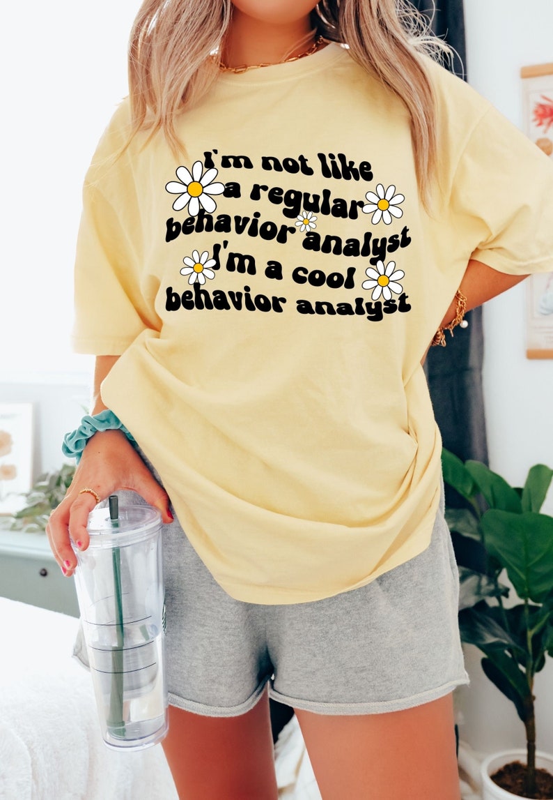 K&ouml;nnte beinhalten: Ein gelbes T-Shirt mit einem G&auml;nsebl&uuml;mchen-Motiv und dem Text "Ich bin nicht wie ein normaler Verhaltensanalytiker Ich bin ein cooler Verhaltensanalytiker".