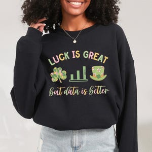 Może przedstawiać: Czarna bluza z nadrukiem graficznym, który głosi "Luck is great but data is better". Grafika zawiera zieloną koniczynę, wykres słupkowy i zielony kapelusz leprechauna.