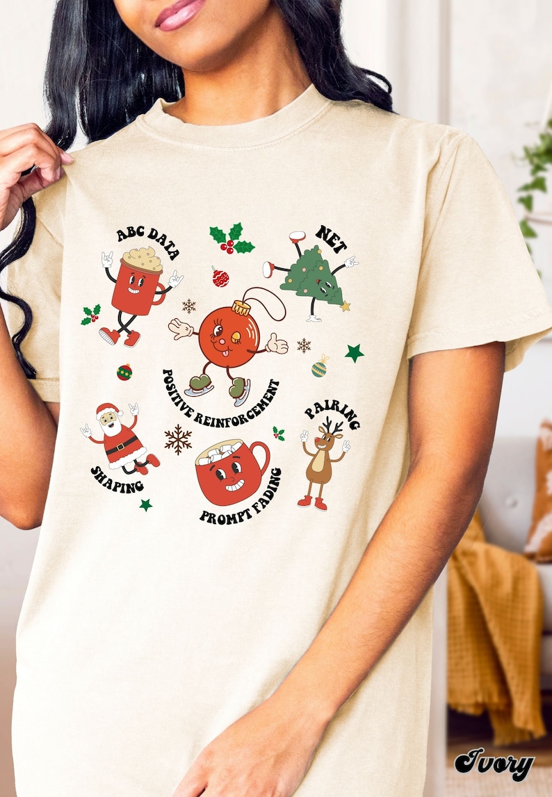 May include: A cream coloured t-shirt with a Christmas themed design featuring cartoon characters and text that says "ABC Data", "Net", "Positive Reinforcement", "Shaping", "Pairing", "Prompt Fading".