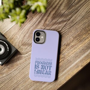 May include: A lavender phone case with a white outline of a wave pattern and the text "Progress is not linear".