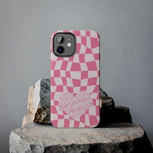 May include: Pink and white checkered phone case with a pink heart that says "Behavior Analyst" in white text.