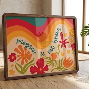May include: A rectangular framed print featuring a wavy, multi-colored background of teal, red, orange, and yellow stripes. The text "progress is not linear" is written in teal, surrounded by stylized red, orange, and yellow flowers.