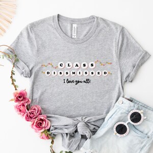May include: Grey t-shirt with the text "CLASS DISMISSED I love you all!" in black lettering. The text is surrounded by a string of colourful circles.