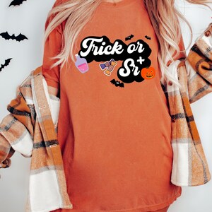 Puede incluir: Una camiseta naranja quemada con el texto "Trick or Sr+" en blanco y negro. El texto est&aacute; en una fuente retro y est&aacute; rodeado de una nube negra. Hay peque&ntilde;as im&aacute;genes de una botella de poci&oacute;n, caramelos, murci&eacute;lagos y una calabaza.