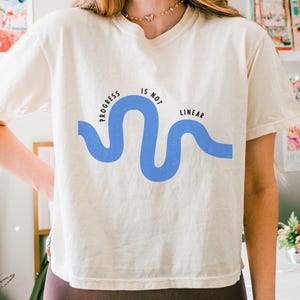 May include: A white t-shirt with a blue wavy line graphic and the text "Progress is not linear".