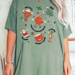 May include: Green t-shirt with a Christmas theme featuring cartoon characters and text that says "ABC Data", "Net", "Positive Reinforcement", "Pairing", "Shaping", "Prompt Fading".