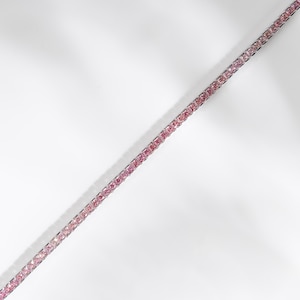 Könnte beinhalten: Ein Tennisarmband mit einer durchgehenden Reihe quadratisch geschliffener rosa Edelsteine, die in einen polierten, silberfarbenen Metallrahmen gefasst sind. Die Steine sind in einer geraden Linie angeordnet und wirken gleichmäßig und glänzend.