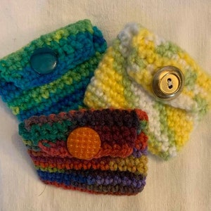 May include: Three crocheted coin purses with different colored stripes and buttons. The purses are made with a variety of colors, including green, blue, yellow, red, orange, and purple.