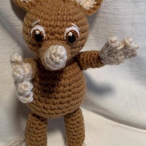 May include: A handmade crochet mouse doll in shades of brown and cream. The mouse has large, expressive eyes, a white nose, and large ears. Its arms and feet are outstretched, giving it a friendly appearance. The doll is approximately 6 inches tall.