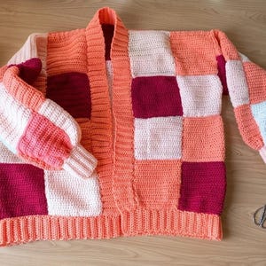 Pode incluir: Cardig&atilde; de croch&ecirc; patchwork feito &agrave; m&atilde;o em tons de p&ecirc;ssego, branco e bord&ocirc;. O su&eacute;ter aberto tem bainha e punhos canelados. Inclui novelos de l&atilde;, agulhas de croch&ecirc; e um caderno.