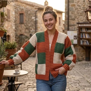 Pode incluir: Uma mulher usando um cardigan de patchwork em tons de laranja, verde e creme. O cardigan aberto &eacute; combinado com jeans azuis. O cen&aacute;rio &eacute; uma cena ao ar livre com edif&iacute;cios de pedra e uma rua de paralelep&iacute;pedos. O cardigan tem um corte descontra&iacute;do.