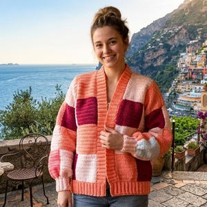 Pode incluir: Um cardigan patchwork em tons de p&ecirc;ssego, rosa e bord&ocirc;. O su&eacute;ter de frente aberta apresenta um design geom&eacute;trico com blocos quadrados e retangulares. As mangas s&atilde;o compridas. O cardigan &eacute; usado ao ar livre.