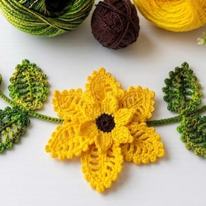 Può includere: Una ghirlanda floreale all'uncinetto fatta a mano con un grande girasole giallo con un centro marrone scuro, affiancato da foglie e boccioli verdi e gialli. La ghirlanda è realizzata in filato ed è adatta per l'arredamento della casa.