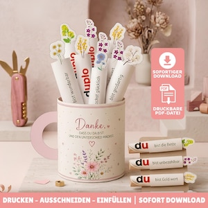 Peut inclure: Un récipient en papier en forme de tasse avec des illustrations florales et du texte allemand, rempli de tubes en papier avec des découpes de fleurs et des phrases comme bist wunderbar et bist großartig. Inclut trois barres emballées.