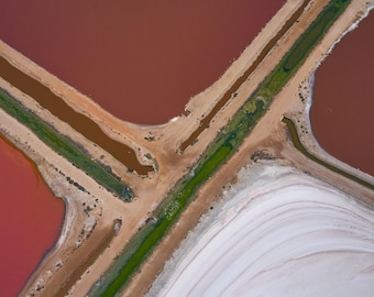 Könnte beinhalten: Eine Luftaufnahme von Salzverdunstungsbecken mit deutlich voneinander abgegrenzten Bereichen aus tief rötlich-rosa Wasser, leuchtend weißen Salzablagerungen und schmalen Erddämmen mit grünen Vegetationsstreifen an den Rändern.