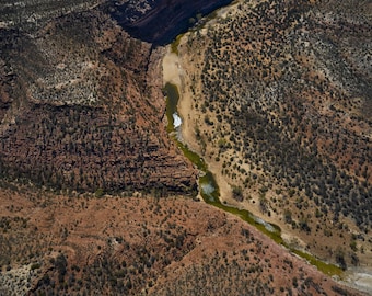 Könnte beinhalten: Luftaufnahme eines Canyons mit einem Fluss, der sich hindurchschlängelt. Die Canyonwände sind rotbraun, und der Fluss ist eine Mischung aus Grün und Weiß. Die umliegende Landschaft ist mit spärlicher Vegetation bedeckt.