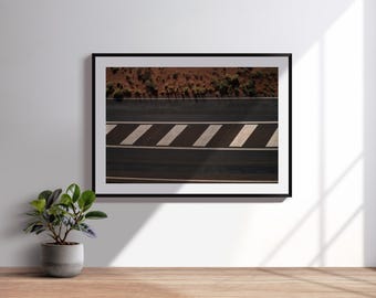 Könnte beinhalten: Gerahmte Fotografie einer Straße mit weißen diagonalen Streifen. Die Straße ist dunkel mit einer braunen und grünen Landschaft oben. Die gerahmte Kunst wird an einer weißen Wand über einer Holzoberfläche ausgestellt.
